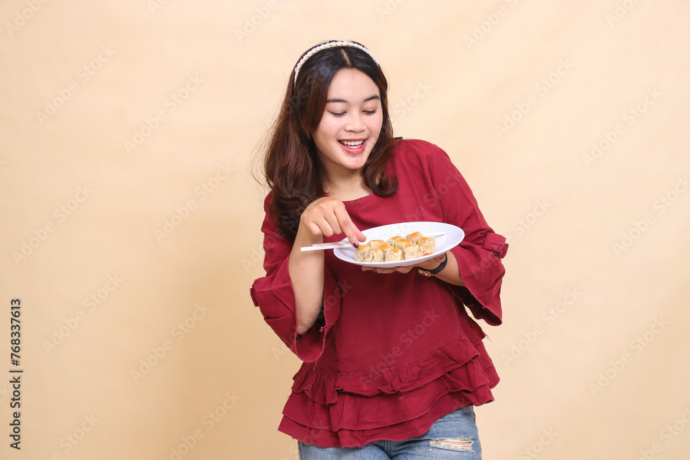 beautiful young indonesia woman in red dress cheerful happy hands with plate containing dimsum (chinese food) and chopsticks while picking it up. used for food, health and lifestyle content beautiful young indonesia woman in red dress cheerful happy hands with plate containing dimsum (chinese food) and chopsticks while picking it up. used for food, health and lifestyle content