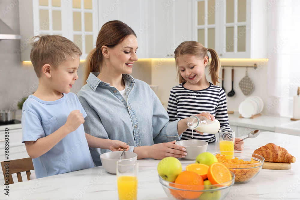 Mother and her little children having breakfast at table in kitchen Mother and her little children having breakfast at table in kitchen