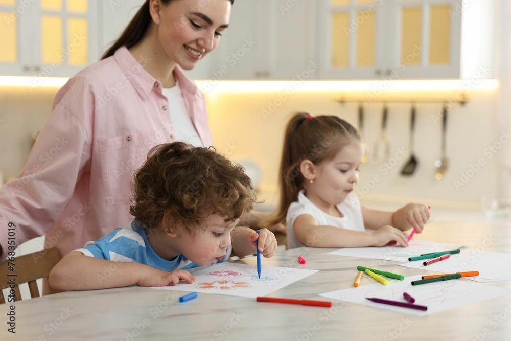 Mother and her little children drawing with colorful markers at table in kitchen Mother and her little children drawing with colorful markers at table in kitchen