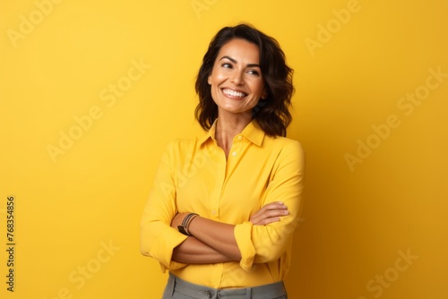 Portrait of a happy businesswoman standing with arms crossed over yellow background