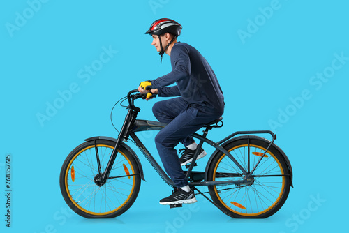 Fototapeta Naklejka Na Ścianę i Meble -  Young man riding bicycle on blue background