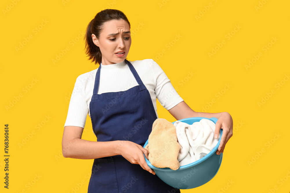 Portrait of tired young housewife in apron with dirty laundry on yellow background Portrait of tired young housewife in apron with dirty laundry on yellow background