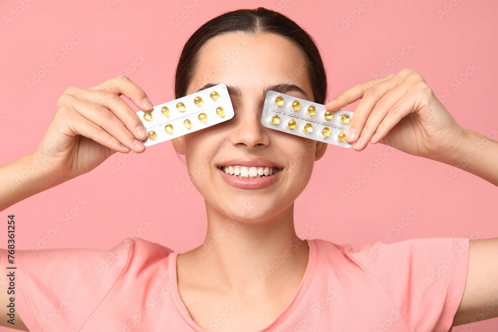 Pretty young woman holding blister packs of vitamin A capsules on pink background - obrazy, fototapety, plakaty 