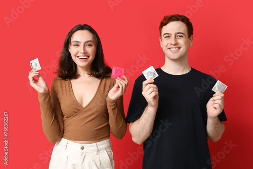 Young couple with condoms on red background. Safe sex concept photo