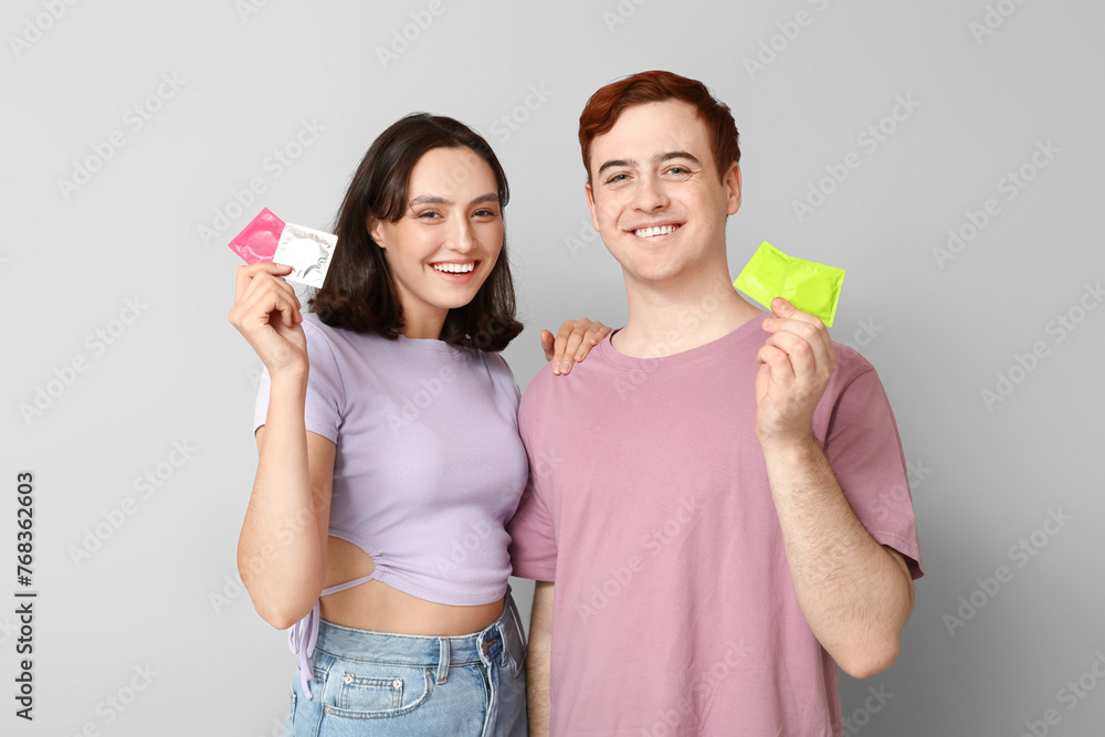 Young couple with condoms on grey background. Safe sex concept Young couple with condoms on grey background. Safe sex concept