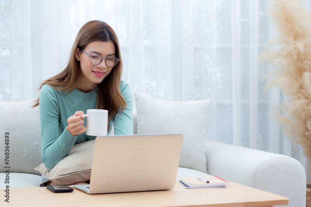 Young asian woman wearing glasses sitting sofa working on laptop computer and drinking coffee in living room at home, woman work from home with telework, freelance working, business and digital life. Young asian woman wearing glasses sitting sofa working on laptop computer and drinking coffee in living room at home, woman work from home with telework, freelance working, business and digital life.