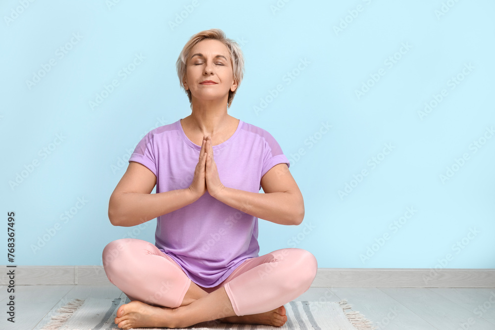 Portrait of meditating mature woman sitting on floor against blue wall Portrait of meditating mature woman sitting on floor against blue wall