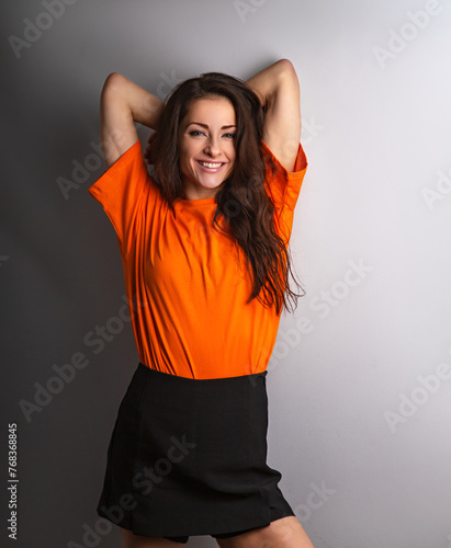 Beautiful young relaxing smiling woman in casual clothing looking with arms behind head in orange casual shirt on grey studio background on empty copy space. Closeup