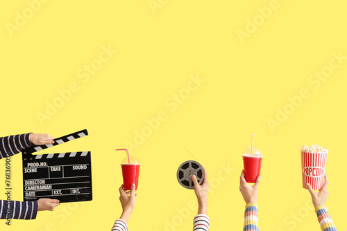 Many hands with movie clapper, bucket of popcorn and drinks on yellow background