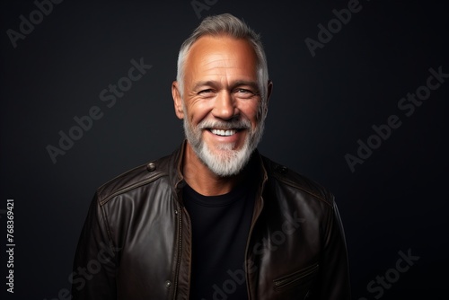 Portrait of a smiling senior man in leather jacket against black background.