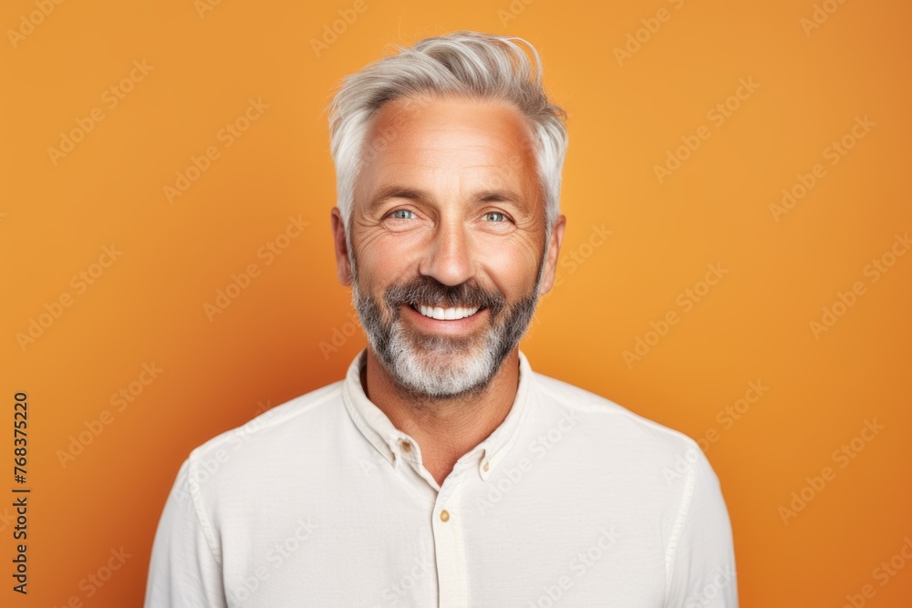 Cheerful mature man looking at camera and smiling while standing against orange background Cheerful mature man looking at camera and smiling while standing against orange background