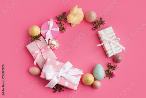 Easter wreath made of gift boxes  eggs and bunny figure on pink background