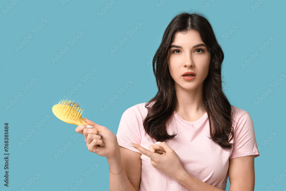 Beautiful young woman pointing at brush with fallen down hair on blue background Beautiful young woman pointing at brush with fallen down hair on blue background