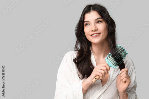 Pretty young woman brushing her hair on grey background