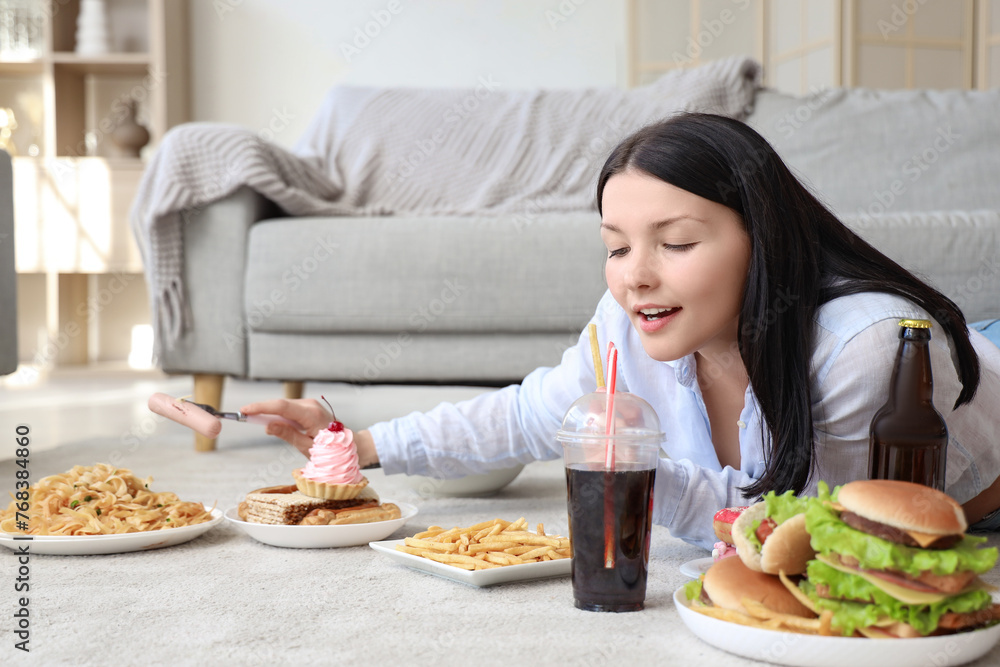 Young woman with unhealthy food lying on floor at home. Overeating concept Young woman with unhealthy food lying on floor at home. Overeating concept