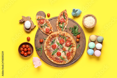 Easter pizza with bunny ears, painted eggs and tomatoes on yellow background