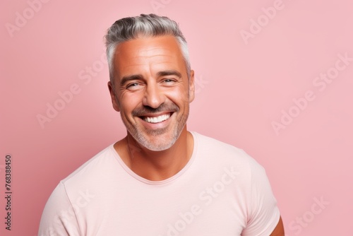 Handsome middle-aged man with grey hair and white beard is looking at camera and smiling, on pink background