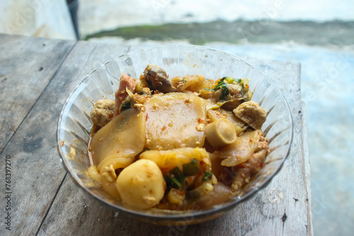 Seblak is a typical Indonesian dish with a savory and spicy taste. cooked with vegetables, sausage, eggs, chicken feet, seafood and processed beef. a bowl of seblak on a wooden table. photo