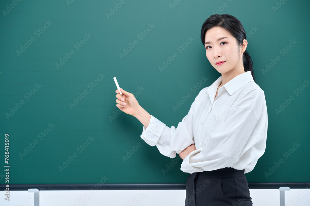 Wearing white heating, a beautiful Asian female teacher is holding a chalk in front of a green chalkboard and giving an Internet lecture with a confident expression and pose. Wearing white heating, a beautiful Asian female teacher is holding a chalk in front of a green chalkboard and giving an Internet lecture with a confident expression and pose.