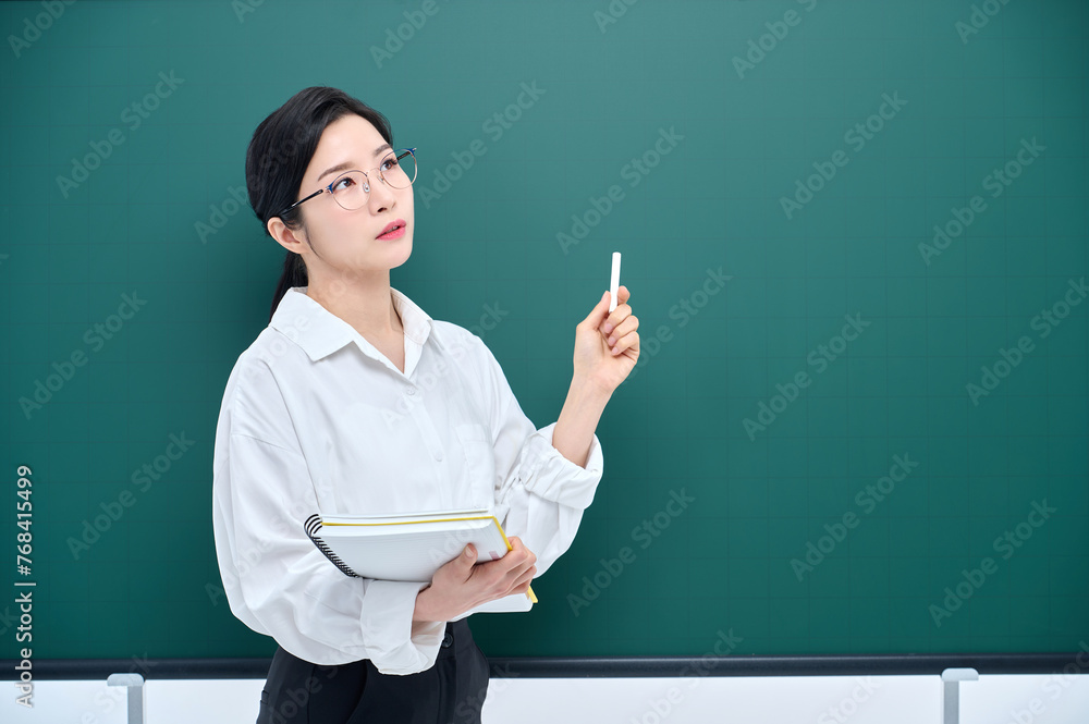 A beautiful Asian female teacher in white heating and glasses is holding a chalk in front of a green chalkboard and giving an Internet lecture with a confident expression and pose. A beautiful Asian female teacher in white heating and glasses is holding a chalk in front of a green chalkboard and giving an Internet lecture with a confident expression and pose.