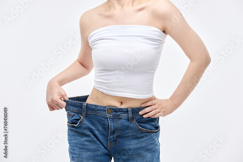A young, slim Asian woman is checking her diet success by wearing jeans in sizes larger than her waist.