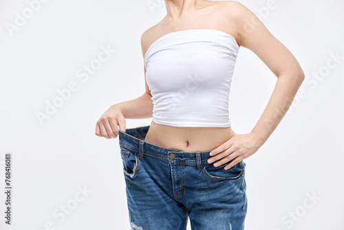 A young, slim Asian woman is checking her diet success by wearing jeans in sizes larger than her waist.