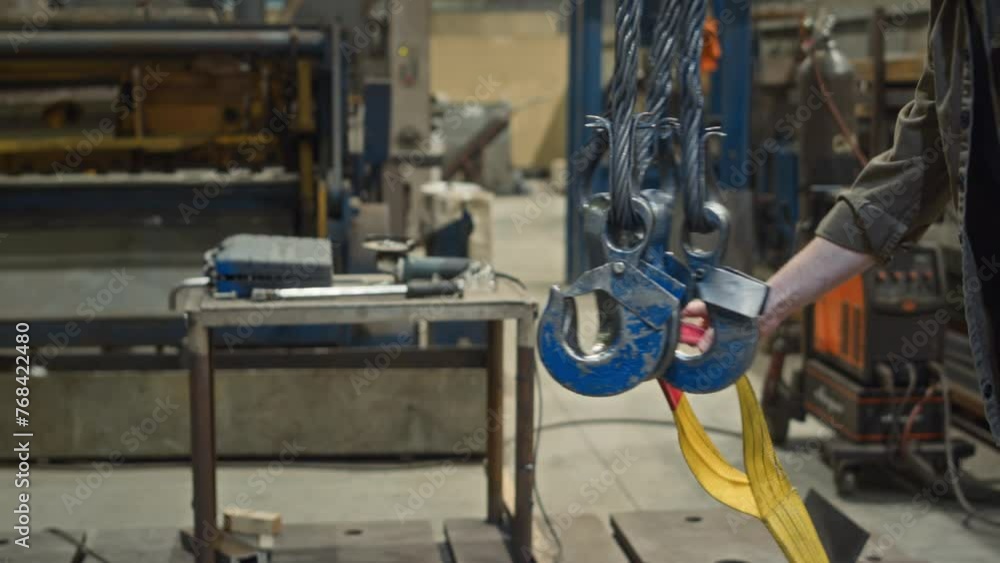 Cropped shot of two unrecognizable male factory workers taking lifting belt slings off crane hooks indoors Cropped shot of two unrecognizable male factory workers taking lifting belt slings off crane hooks indoors