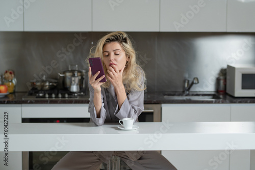 Sexy woman reading message or bad new at smartphone in the kitchen. Woman wearing pajama drink coffee in home kitchen.
