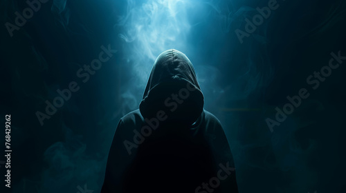 A hacker is wearing a hoodie and standing in a dark background