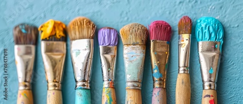  A line of paintbrushes aligned with a blue background, featuring paint splatters on the bristles