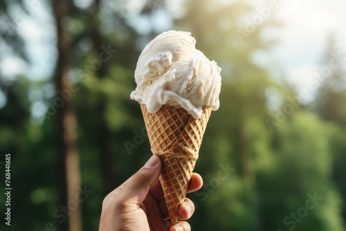 Young woman holding ice cream cone on sunny summer day with nature background in close-up view