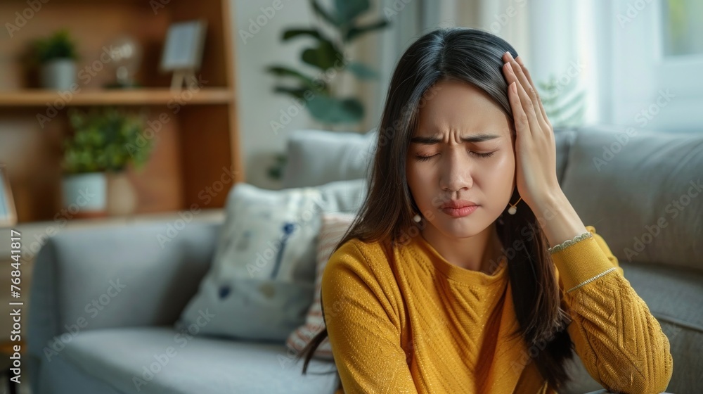 Asian girl suffering from migraine pain in comfortable living room setting. Asian girl suffering from migraine pain in comfortable living room setting.