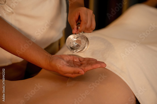 Closeup masseur hand pouring aroma oil on woman back. Masseuse prepare oil massage procedure for customer at spa salon in luxury resort. Aroma oil body massage therapy concept. Quiescent