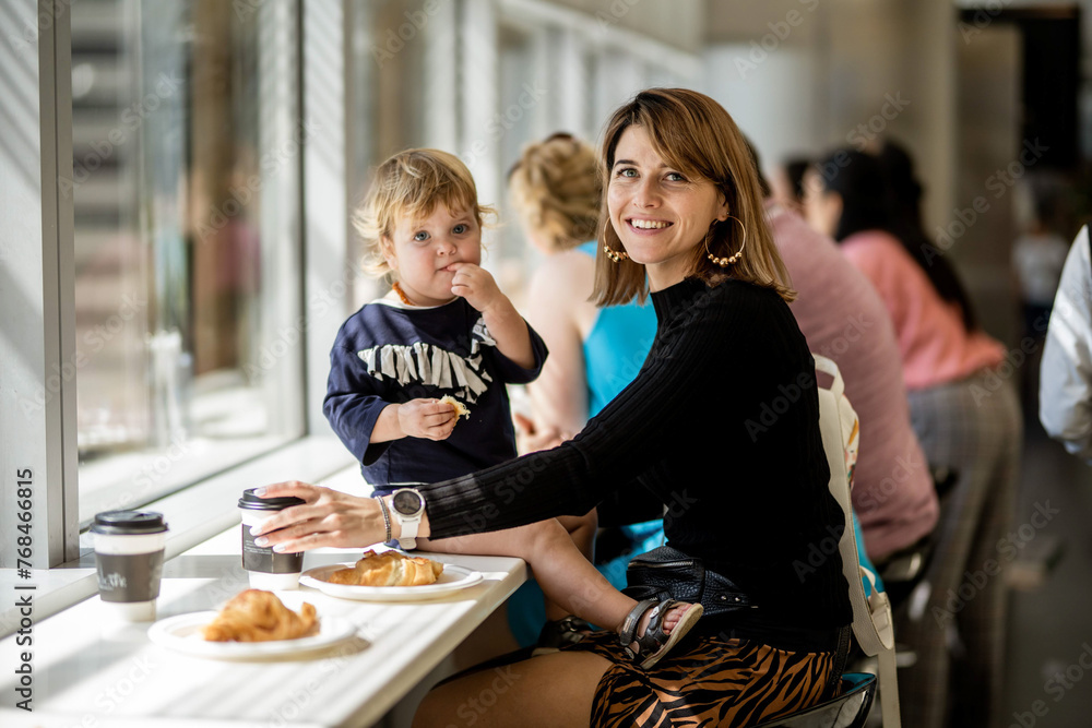 Φωτογραφία Dubai,  Unite dArab Emirates - October 19, 2019 - A woman and a child are sitting at a cafe table by a window; the woman is smiling at the camera, and the child is eating