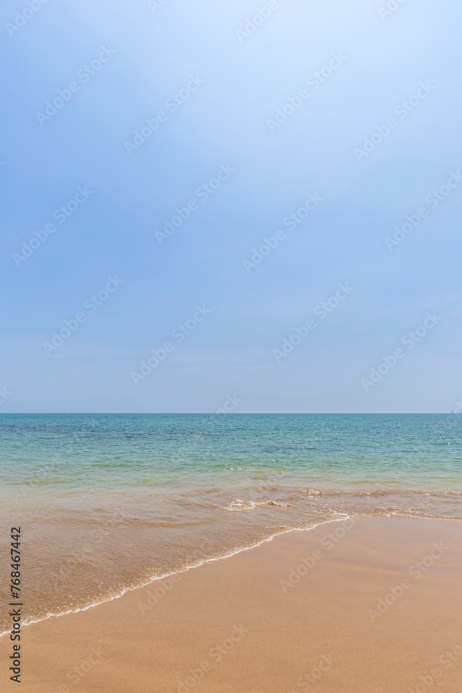 Front view of a small wave crashing on a sandy beach, sea and blue sky on a sunny day. Natural tropical travel and vacation background with copy space.