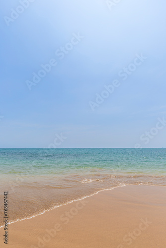 Fototapeta Naklejka Na Ścianę i Meble -  Front view of a small wave crashing on a sandy beach, sea and blue sky on a sunny day. Natural tropical travel and vacation background with copy space.