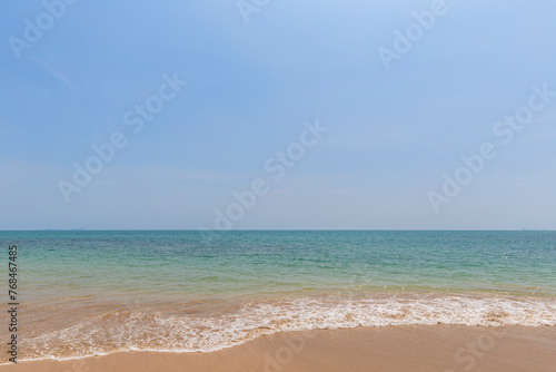 Front view of a small wave crashing on a sandy beach  sea and blue sky on a sunny day. Natural tropical travel and vacation background with copy space.