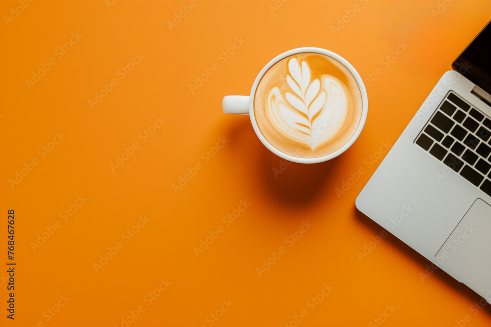 tasse à café blanche remplie d'un art caffe latte à la mousse blanche, à côté d'un ordinateur portable ouvert, laptop et café sur un fond orange espace négatif copy space - obrazy, fototapety, plakaty 
