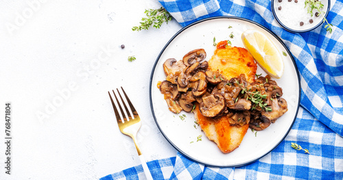 French breaded chicken breast steak with mushrooms and onion sauce with white wine and thyme on plate, white  table background, top view