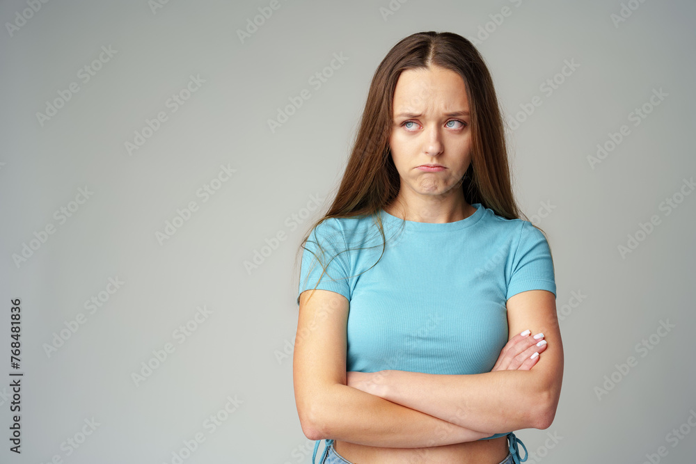 Obraz premium Portrait of sad displeased offended young woman in blue T-shirt on gray background