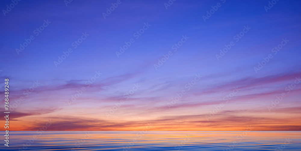 Idyllic sunset sky background over sea with colorful sunlight reflection on motion blur of flowing water surface in panoramic view, tranquil seascape scene 