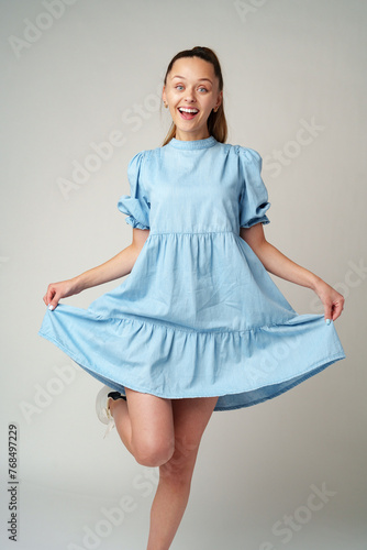 Young happy smiling woman in a light blue dress on a gray background