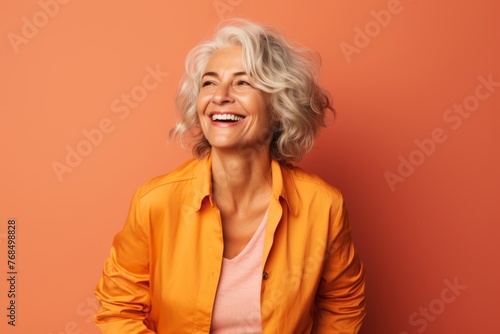 Portrait of happy senior woman with short wavy blonde hair on orange background.
