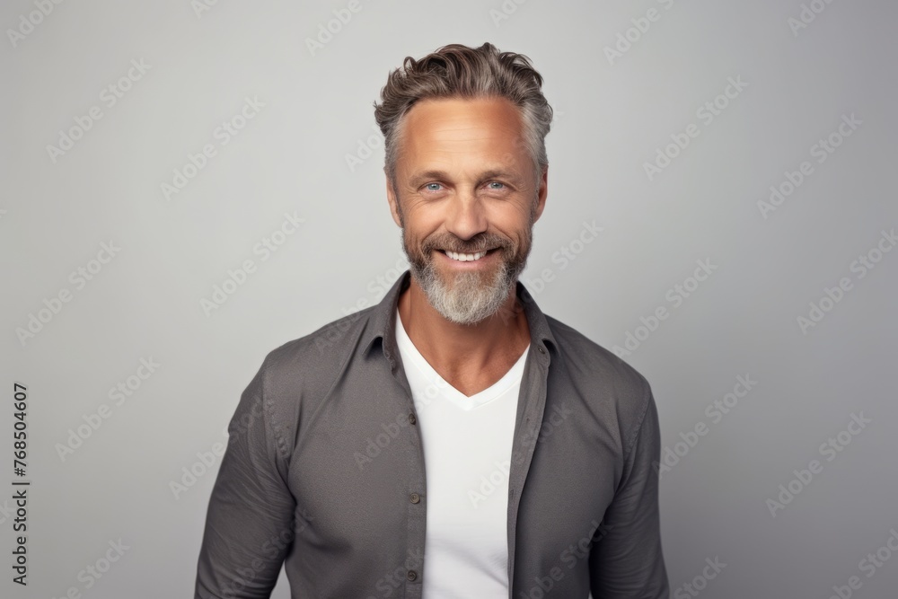 Handsome mature man looking at camera and smiling while standing against grey background Handsome mature man looking at camera and smiling while standing against grey background