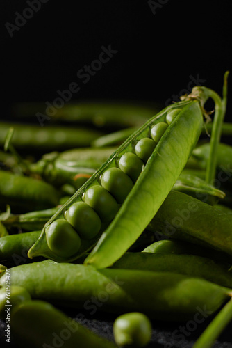 Open pod of young green peas with round peas close-up,Indoor black background and wooden bowl