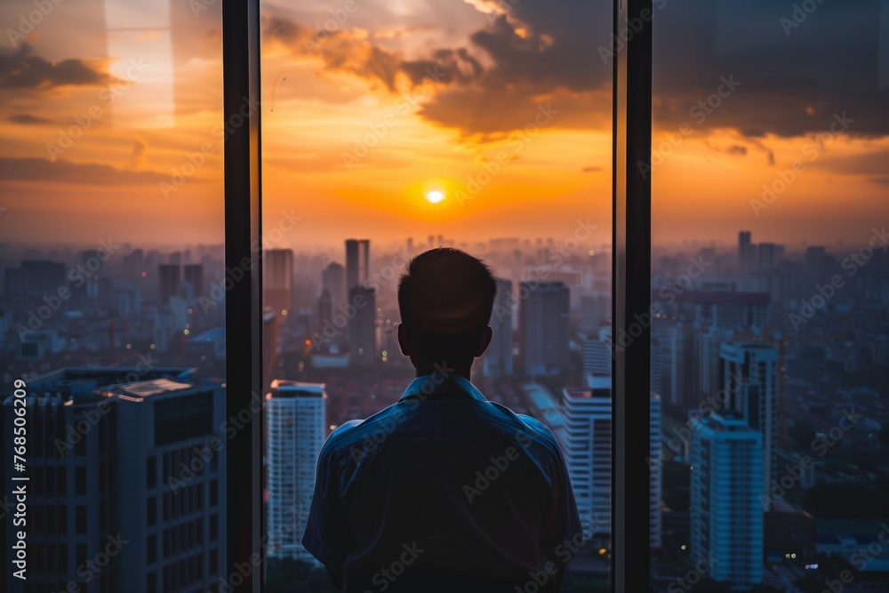 Fototapeta premium man looking at cityscape from office during sunset