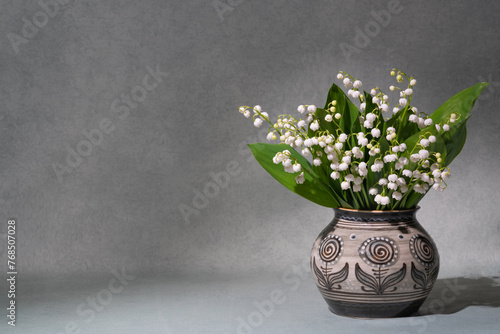 A small bouquet of fresh spring flowers. Lilies of the valley in a light vase isolated on a gray background. Lots of space for text. still life, postcard, gift photo