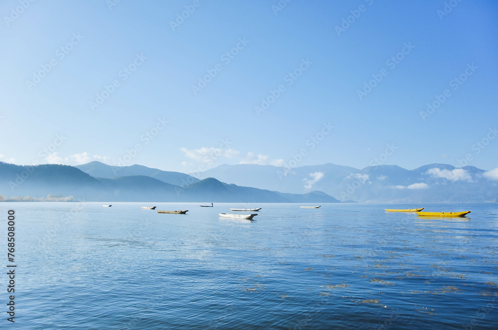 A group of small wooden fishing row boat on blue Lugu Lake. Lakeside blue water in the distance blue sky with white fluffy clouds