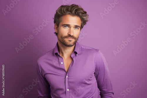 Handsome young man in purple shirt looking at camera while standing against purple background