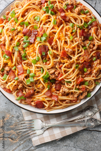 American style Spaghetti pasta with bacon, minced meat, cheddar cheese, onion and spicy tomato sauce close-up in a plate on the table. Vertical top view from above